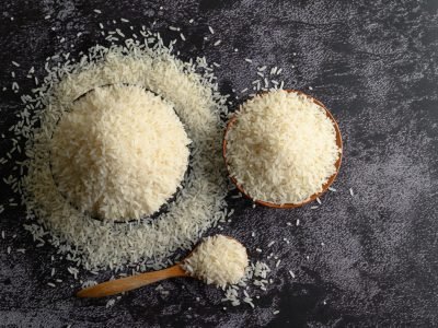 Milled rice in a bowl and a wooden spoon on the black cement floor. Top view